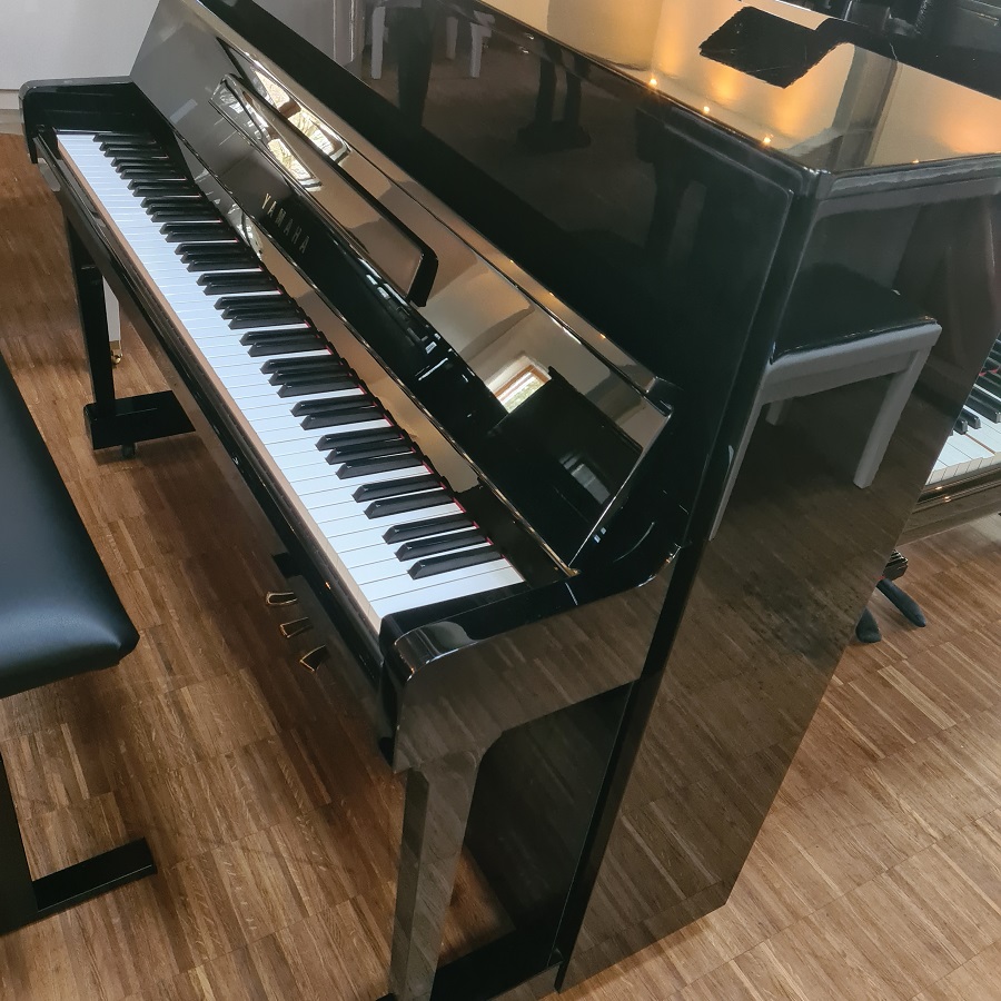 Schwarzes Yamaha Klavier mit glänzender Oberfläche steht auf Holzfußboden in hellem Raum mit Stuhl und Spiegel.​​​​​​​​​​​​​​​​​​​​​​​​​​​​​​​​​​