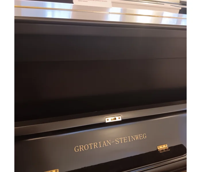 Goldener Schriftzug „Grotrian-Steinweg“ auf schwarzem Klaviergehäuse, Detailaufnahme.