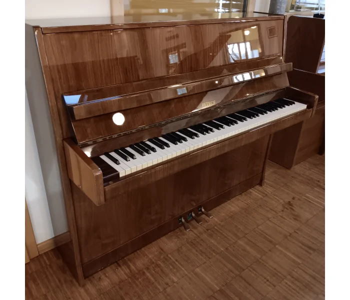 Petrof Klavier 115 in Nussbaum poliert, Schrägansicht mit sichtbarer Klaviatur und Pedalen.