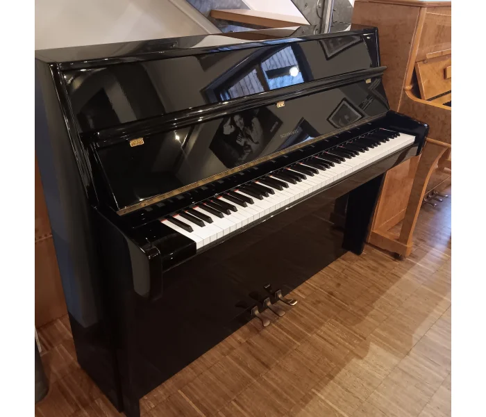 Schwarzes Schimmel-Klavier mit geöffneter Tastaturklappe und drei Pedalen, schräg von oben.